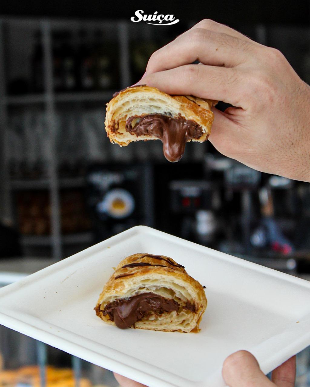 Croissant recheado de chocolate sendo partido ao meio sobre um prato branco.