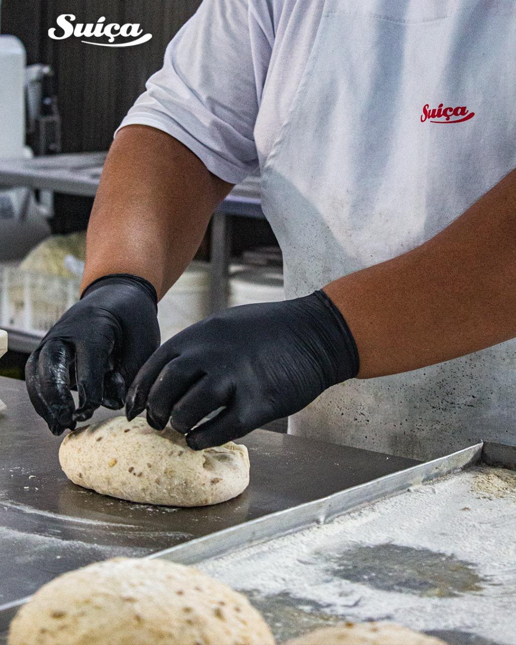 Padeiro da Suíça modelando à mão um pão integral sobre a bancada enfarinhada.