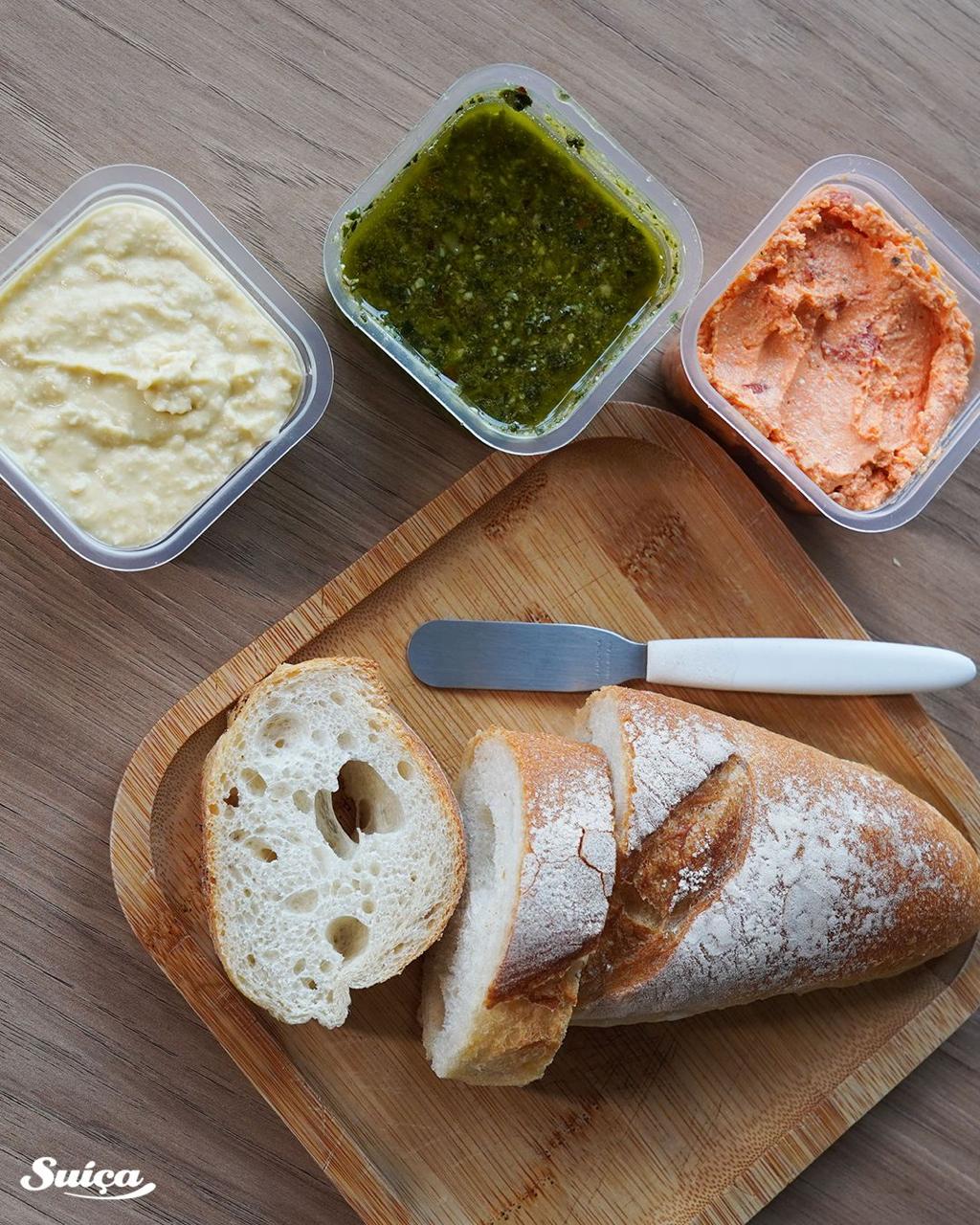 Três patés em potes ao lado de um pão italiano fatiado sobre a tábua.