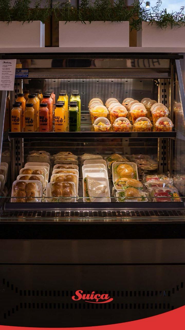 Vitrine refrigerada da Suíça com sucos, saladas de fruta, pães e sanduíches.